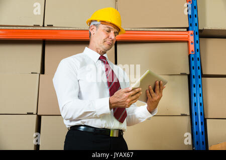 Businessman In Hardhat Looking At Digital Tablet In Warehouse Stock Photo