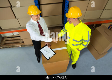 Smiling Warehouse Manager And Worker Shaking Hands In Warehouse Stock Photo