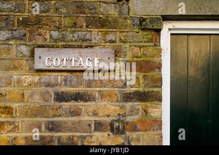 Cottage wooden sign on a brick wall. Landscape format. Stock Photo
