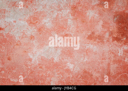 Close-up of a weathered and aged concrete wall, bleached red paint partly peeled off. Texture background with vignette. Stock Photo