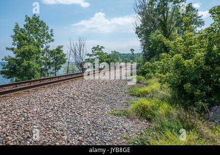 Railroad tracks on the edge of Lake Champlain with trees and crushed stone and a blue sky with a few clouds Stock Photo