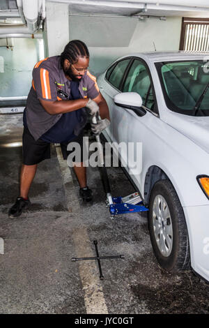 Miami Beach Florida,parking garage,roadside assistance,Black man men male,flat tire,repairing,job,jack,jacking car,FL170430056 Stock Photo