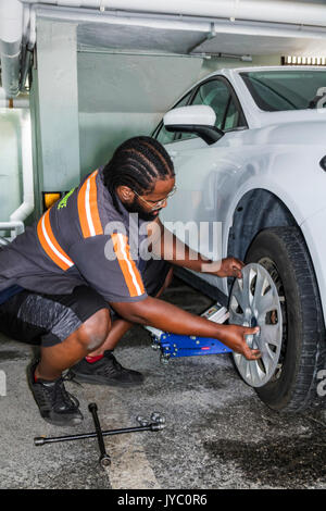 Miami Beach Florida,parking garage,roadside assistance,Black man men male,flat tire,repairing,job,car,fixing,FL170430058 Stock Photo