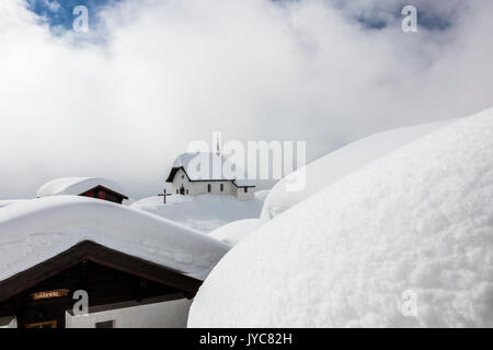 Clouds frame the mountain huts and church covered with snow Bettmeralp district of Raron canton of Valais Switzerland Europe Stock Photo