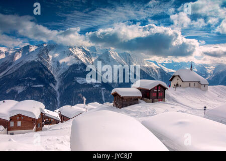 Clouds and blue sky frame the mountain huts covered with snow Bettmeralp district of Raron canton of Valais Switzerland Europe Stock Photo