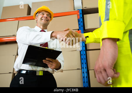 Happy Manager Holding Clipboard Shaking Hands With Warehouse Worker Stock Photo