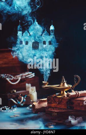 Dark dreamy still life with magic lamp and mystic smoke forming an arabic castle. Boxes filled with treasure and jewelry on a background. Stock Photo