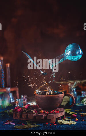 Flying potion bottle with pouring liquid in a magical still life. Brewing enchanted tea. Wooden background with magical supplies. Copy space. Stock Photo