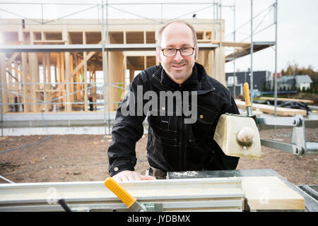 Male Carpenter Smiling While Using Table Saw To Cut Plank Stock Photo
