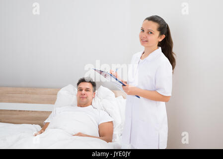 Female Doctor With Clipboard Standing Near Patient Lying On Bed Stock Photo