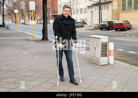 Portrait Of A Man Trying To Walk On Street With The Help Crutches Stock Photo