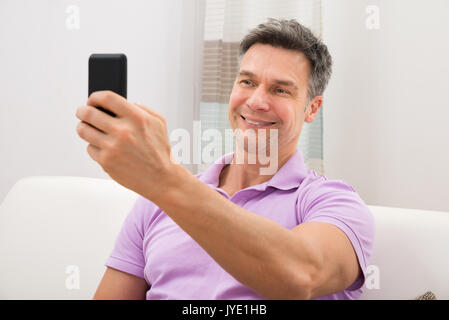 Portrait Of A Happy Man Sitting On Couch Holding Cellphone Stock Photo
