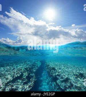 Over and under water surface seascape, sunlight with cloudy blue sky and split by waterline a natural trench in the reef underwater, Pacific ocean Stock Photo