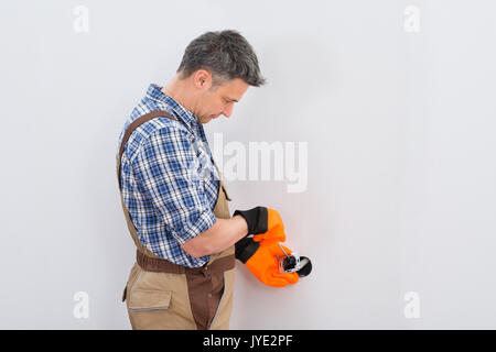 Portrait Of A Technician Wearing Glove Fixing Socket With Screwdriver On Wall Stock Photo