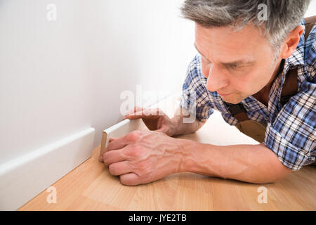 Close-up Of A Carpenter Leaning On Floor Applying Skirting On Wall Stock Photo
