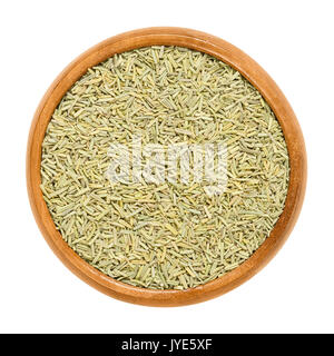 Rosemary dried in wooden bowl. Sliced needle like leaves of Rosmarinus officinalis. Herb with aromatic olive green leaves and a bitter taste. Stock Photo