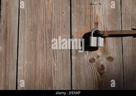 The new iron lock on an old metal fixing hangs on a high wooden gate, a texture, a horizontal color photo. Stock Photo