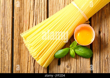 Dried spaghetti and raw egg on wooden background Stock Photo