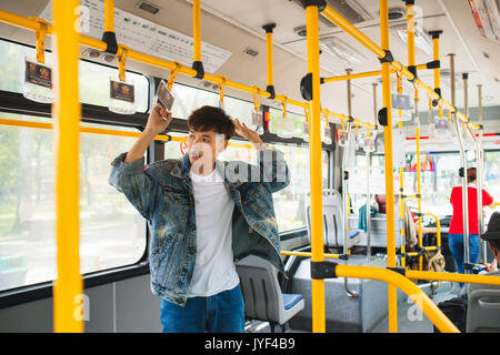 Asian man taking public transport, standing inside bus. Stock Photo