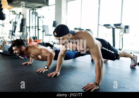Two strong men doing push-ups in gym Stock Photo
