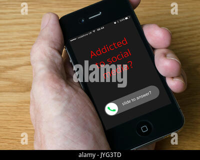 Handheld iPhone mobile phone showing message 'Addicted to social media?' concept image. Stock Photo
