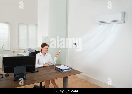 Happy Businesswoman Operating Air Conditioner With Remote Control In Office Stock Photo