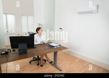 Happy Businesswoman Operating Air Conditioner With Remote Control In Office Stock Photo