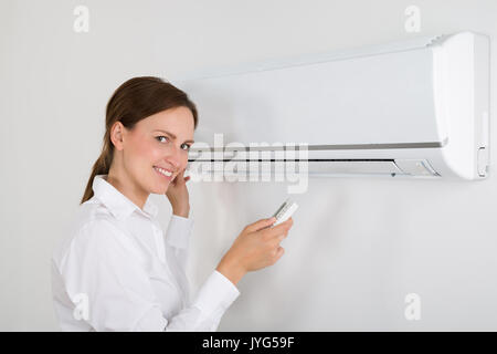 Happy Businesswoman Operating Air Conditioner Mounted On White Wall In Office Stock Photo