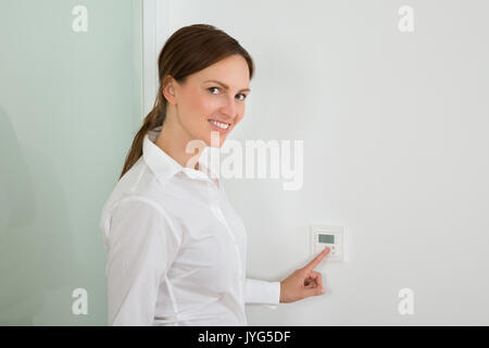 Beautiful Young Businesswoman Setting The Temperature On Digital Thermostat Stock Photo