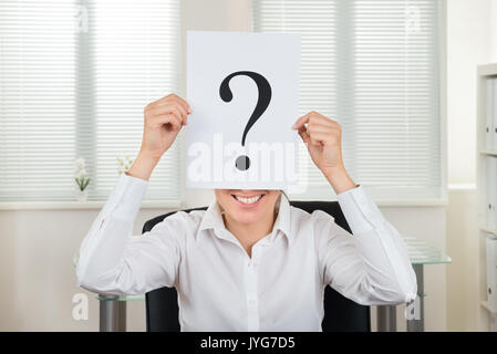 Happy Businesswoman Showing Question Mark On Paper At Desk Stock Photo
