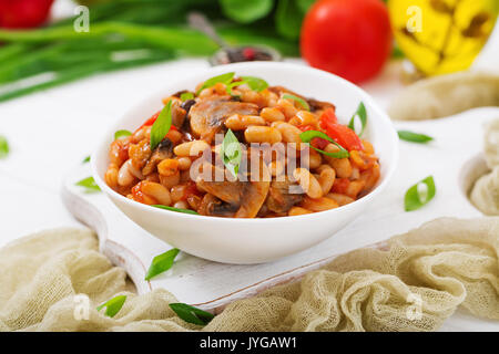 Stewed white beans with mushrooms and tomatoes with spicy sauce in a white bowl. Stock Photo