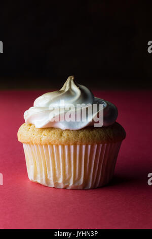 Single lemon custard centred eggwhite meringue decorated sponge cupcake closeup isolated on vertical red background - space for your text Stock Photo