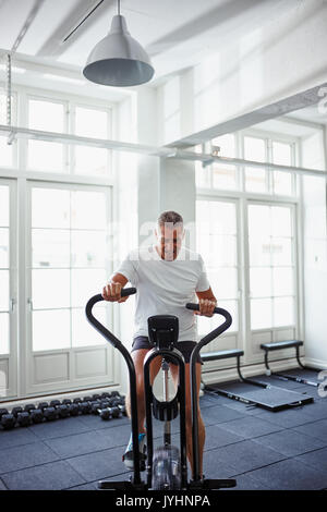 Determined mature man in sportswear pushing himself riding a stationary bike while working out alone at the gym Stock Photo