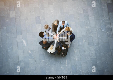 From above black and white business people having teambuilding in hall of office standing with hands stacked.
