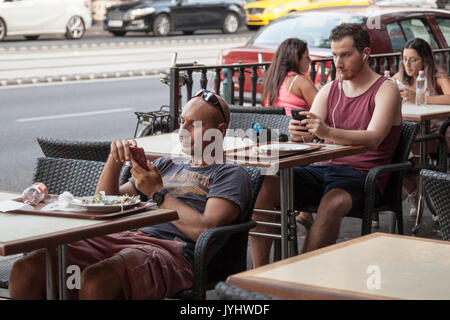 BUDAPEST, HUNGARY - AUGUST 11, 2017: two young caucasian men using their smartphones while sitting at bar tables in the center of Budapest, Hungarian  Stock Photo