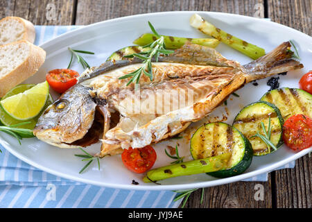 Grilled gilthead seabream with mixed rosemary vegetables served on an oval white fish plate Stock Photo