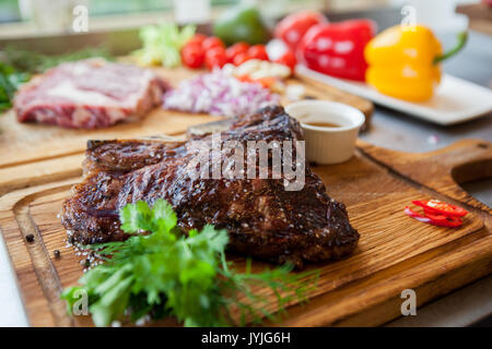 Thick juicy portions of grilled roasted meat on a wooden Board with vegetables Stock Photo