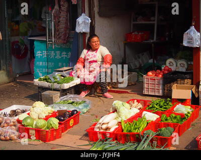 Beijing, China - 10 October, 2016: A woman sits outside her vegetable stall in a Beijing hutong Stock Photo