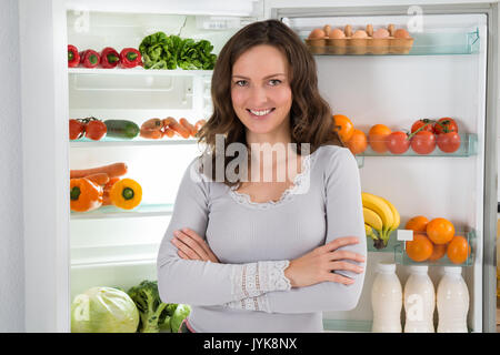 Young Happy Woman With Armcrossed In Front Of Open Fridge With Healthy Food Stock Photo