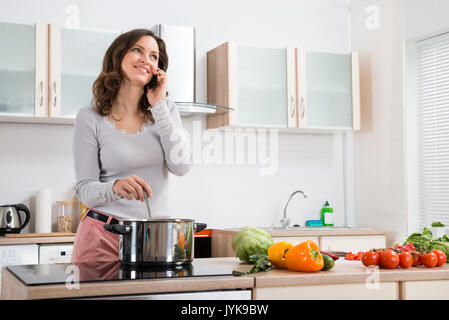 Happy Woman Talking On Mobile Phone While Cooking In Kitchen Stock Photo