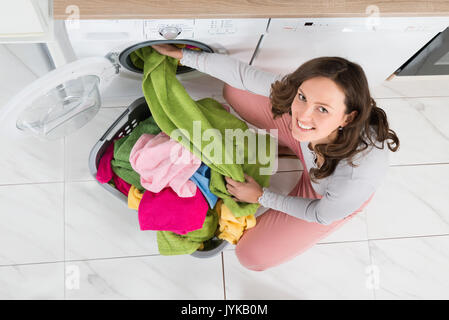 High Angle View Of Young Woman Loading Multi-colored Clothes In Washer Stock Photo