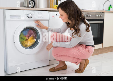 Young Woman Looking At Clean Clothes Out Of Washing Machine In Kitchen  Stock Photo - Alamy