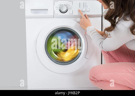 Close-up Of Young Woman Pressing Button Of Washing Machine In Kitchen Stock Photo