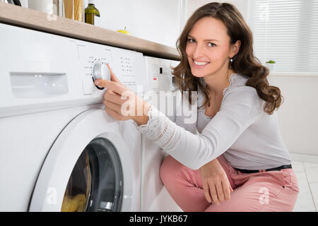 Close-up Of Young Woman Pressing Button Of Washing Machine In Kitchen Stock Photo