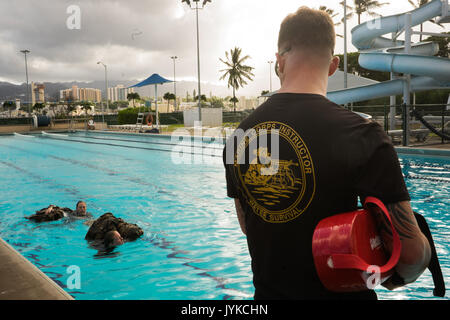 U.S. Marine Corps Staff Sgt. Sean Hutchinson, a Marine Corps Instructor of Water Survival with U.S. Marine Corps Forces, Pacific, watches over Marines swimming during a water survival course aboard Joint Base Pearl Harbor-Hickam, Hawaii, Aug. 11, 2017. The purpose of the water survival program is to ensure combat readiness by providing Marines the ability to survive a waterborne mishap. (U.S. Marine Corps photo by Lance Cpl. Maximiliano Rosas) Stock Photo