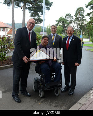 Invictus Games CEO Michael Burns, along with Canada’s Minister of Veteran Affairs Honourable Kent Hehr and his Deputy Minister General (Retired) Walter Natynczyk present David Coker, President of the Fisher House Foundation with a keepsake Invictus Games Flag, Aug. 15, 2017 at the Fisher House near Landstuhl Regional Medical Center. Families of patients like Canadian Cpl. (retired) Chris Klodt, who was wounded in battle in Afghanistan, can stay at the Fisher House at no cost while their service member is being treated at LRMC. (U.S. Army photo by Visual Information Specialist Elisabeth Paque/R Stock Photo