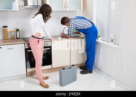 Young Woman Looking At Plumber In Overall Fixing Sink In Kitchen Stock Photo