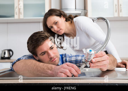 Young Woman Looking At Plumber Fixing Steel Tap In Kitchen Sink Stock Photo