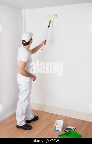 Young Painter In White Uniform Painting With Paint Roller On Wall Stock Photo