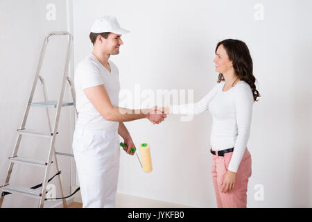 Young Beautiful Woman Shaking Hands To Painter With Paint Roller At Home Stock Photo